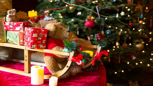Christmas teddy bear sitting on a wooden slay in front of a Christmas tree